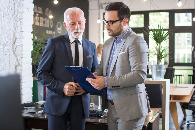 Junge und alte Geschäftsleute in formalen Anzügen, die ein Dokument bei einem Treffen im Büro besprechen